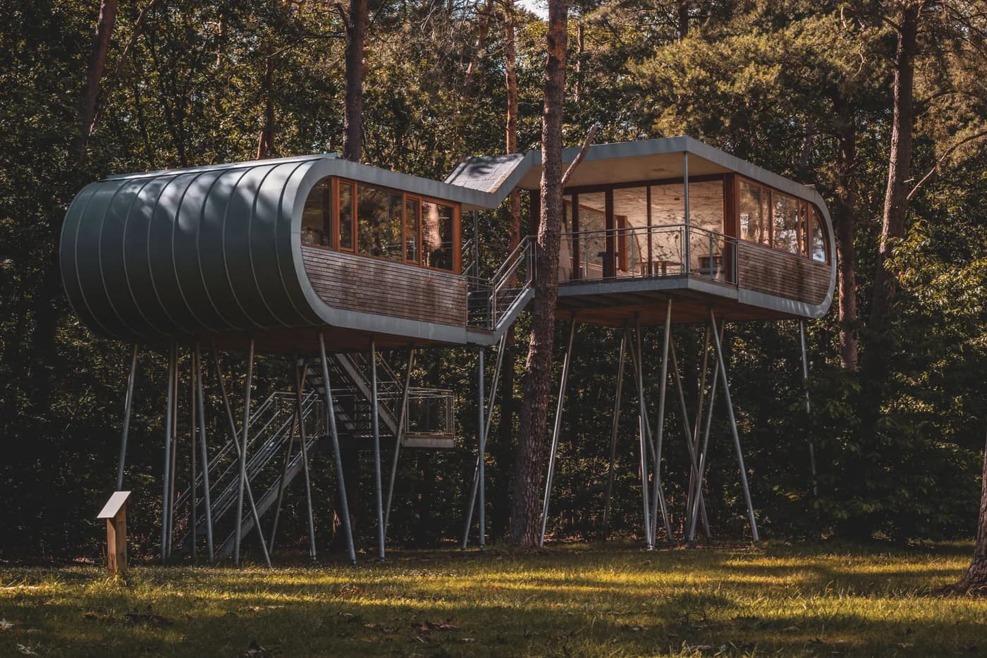 BookNoFees Imagem de exemplo: duas casas na árvore modernas, assentes em pilares, com escadas metálicas entre as árvores da floresta