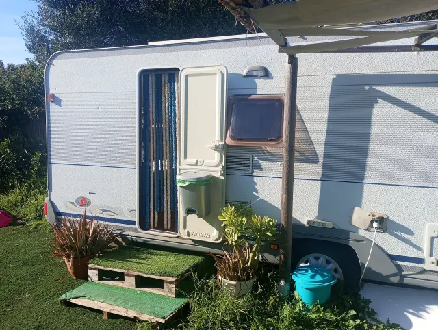 BookNoFees: casa de férias em El Palmar De Vejer – Exterior de uma caravana antiga com a porta aberta, toldo e vasos de plantas na relva