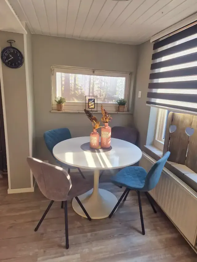 BookNoFees: casa de férias em Domburg – Sala de jantar com uma mesa redonda branca, cadeiras azuis e cinzentas e uma janela com vista para a floresta