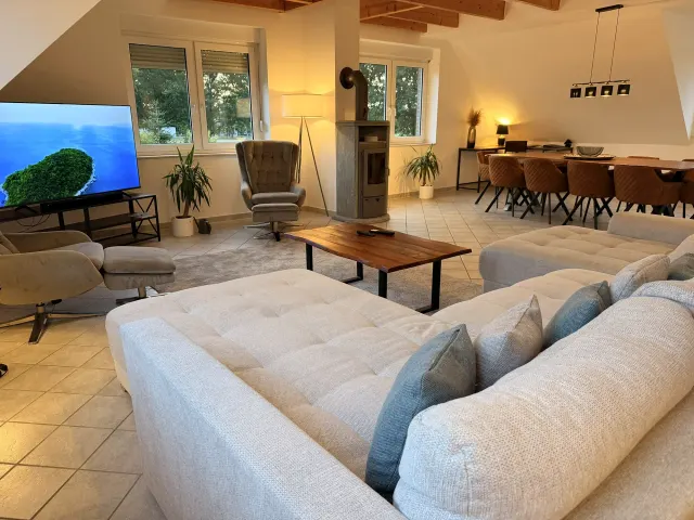 BookNoFees: casa de férias em Stuhr – Sala de estar com sofá em forma de L, salamandra e zona de refeições com mesa de madeira
