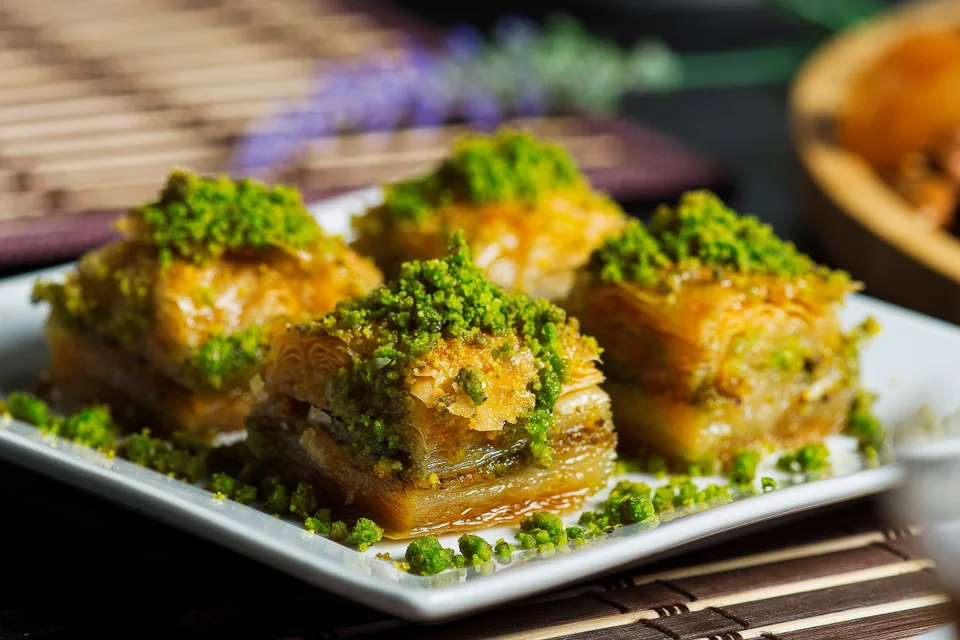 Example photo: Four pieces of layered baklava topped with crushed pistachios on a white plate